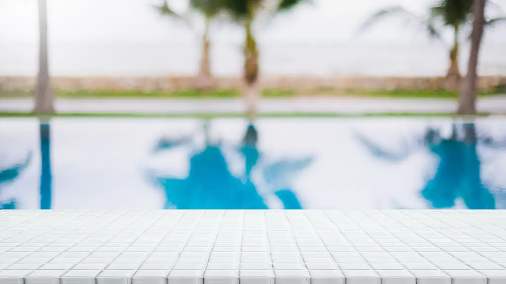 Weiße Mosaikfliesen am Rand eines Pools mit Palmen im Hintergrund