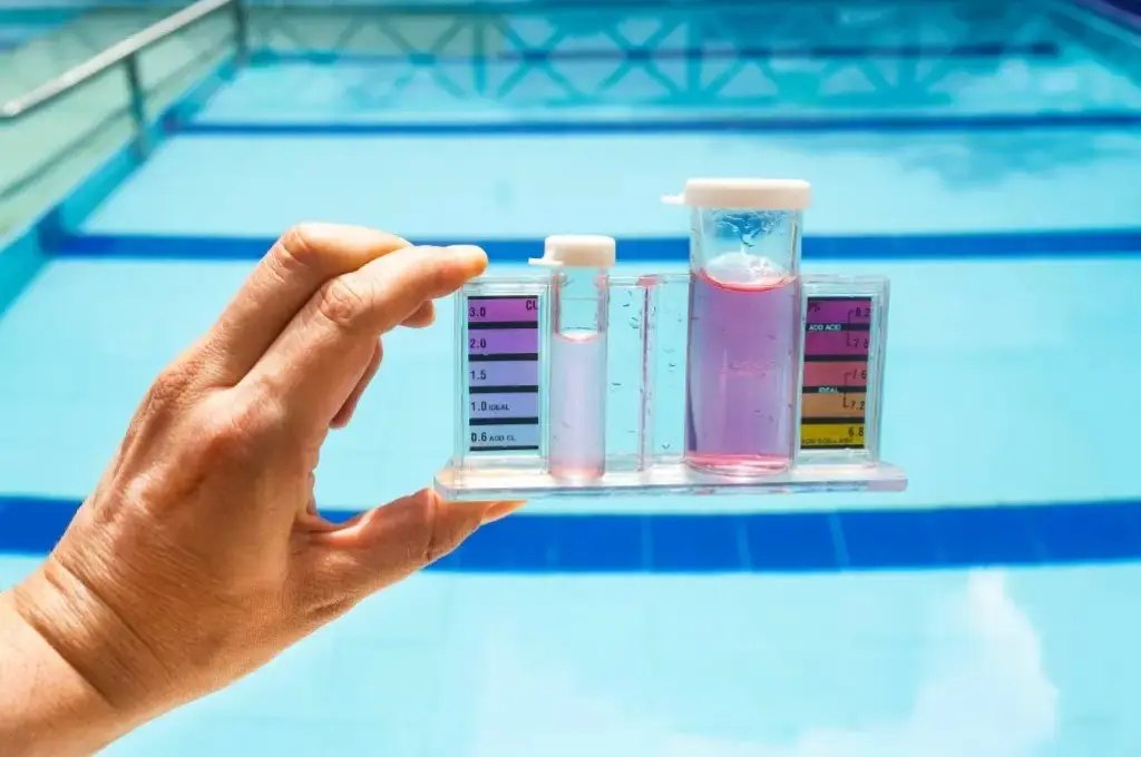 Hand hält ph-Mess-Set mit farbigen Skalen und Messwerten vor Pool im Hintergrund